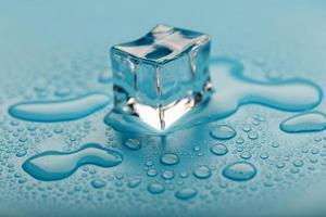 cubo de hielo con gotas de agua sobre un fondo azul. El hielo se está derritiendo. foto