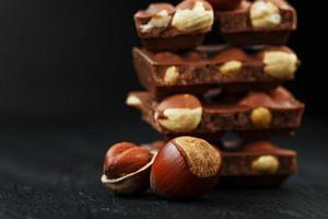 Chocolate with hazelnuts in the form of a tower on a dark background, surrounded by nuts in the shell and peeled. photo