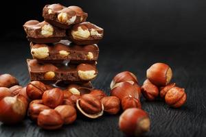 Chocolate with hazelnuts in the form of a tower on a dark background, surrounded by nuts in the shell and peeled. photo