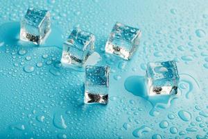 cubos de hielo con gotas de agua esparcidas sobre un fondo azul, vista superior. foto