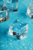 los cubos de hielo están esparcidos con gotas de agua esparcidas sobre un fondo azul. de cerca. foto