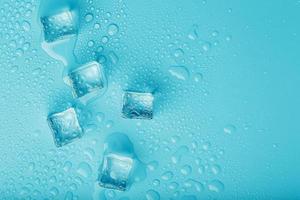 Ice cubes with water drops scattered on a blue background, top view. photo