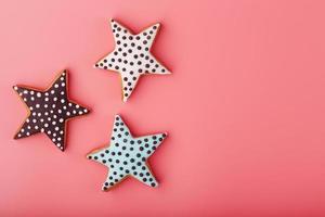 se hace un primer plano de tres galletas de jengibre glaseadas caseras en forma de estrellas sobre un fondo rosa. galletas hechas a mano. foto