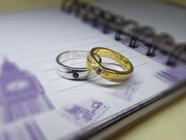 A pair of wedding rings and engagement rings made of silver and yellow gold placed on a notebook photo