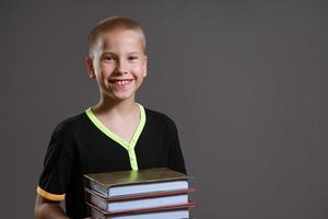 Cheerful boy holding a stack of books on a gray background photo