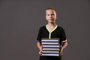 niño escolar sosteniendo una pila de libros sobre un fondo gris foto