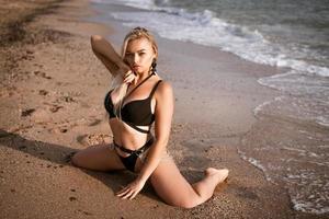 Beautiful young woman sitting posing in a swimsuit on the seashore photo