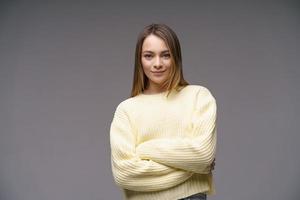 Portrait of cute young woman in yellow sweater on gray background photo
