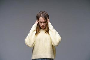 mujer joven sosteniendo su cabeza en suéter amarillo sobre fondo gris foto