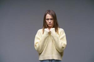 joven disgustada con suéter amarillo de fondo gris tomándose de la mano en puños foto