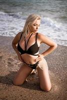 Beautiful woman in black swimsuit posing on the shore photo