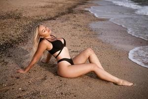 Sexy woman sitting by the sea in a black swimsuit photo