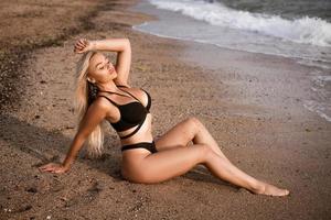 Beautiful woman in black swimsuit posing on the shore photo