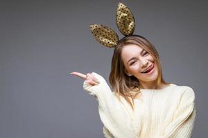 Young woman in rabbit ears shows tongue and finger to the side on background photo