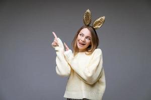 Young woman in rabbit ears shows tongue and finger to the side on background photo