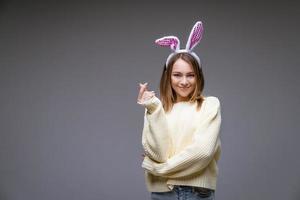 una joven sonriente con orejas de conejo muestra un mini corazón con los dedos foto