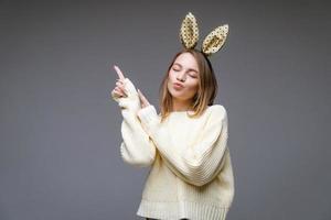 beautiful young woman in bunny ears shows her finger to side on background photo