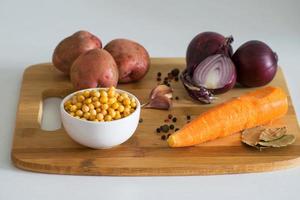 Ingredients for vegetable soup. Ingredients for pea soup - potatoes, carrots, onions, garlic, peppers and peas on a wooden board. Rustic style. photo