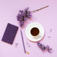 una taza de té, cuadernos, un bolígrafo, un ramo de lilas sobre un fondo morado. flores de primavera moradas. pausa para el té en el trabajo blogger u oficinista foto