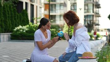 Traveling friends sit with luggage outside and look at a small globe video