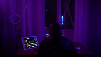 Young woman in a dark purple room uses a laptop video