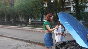 deux jeunes femmes regardent sous le capot d'une voiture video