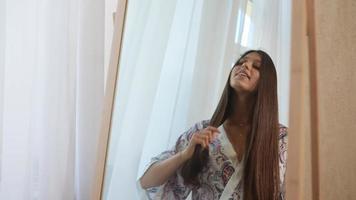 Young beautiful woman brushes long hair and smiles video