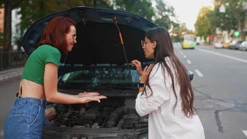 Two young women look under the hood of a car