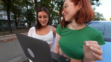 två ung kvinnor se på en bärbar dator närliggande en avstannade bil video