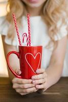 A red mug with a heart pattern with cocoa and paper tubes in the hands of a woman. Valentine's Day Concept photo