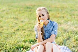 retrato de una mujer joven bebiendo jugo de naranja en un vaso en un picnic de verano en el parque al aire libre foto