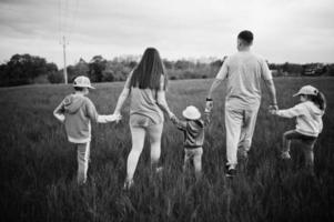 atrás de caminar padres con tres niños divirtiéndose juntos en el prado. foto