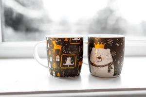 Two cups with a hot drink, Christmas decor, illuminations on a windowsill with winter background, concept of family winter holidays photo