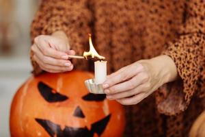 holidays and leisure concept - woman's hand with matches lighting candles at home on halloween. painted pumpkins on a background. horror theme and Hallowe'en. photo