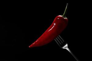side view of red pepper on fork on black background. Domestic cultivation. Fresh vegetables. Vegetarian dinner. Paprika on a fork. Isolated from background. photo