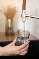 Woman filling drinking glass with tap water on the kitchen. Concept of clean drinking tap water at home. Pouring fresh drink. Water quality check concept. The concept of saving, problems with water photo