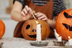 niña enciende una vela para halloween. niña en traje de bruja con calabaza tallada con una cara hecha por un niño. familia feliz preparándose para halloween. enfoque selectivo foto