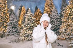 cute caucasian blonde girl in white eco fur coat, hat and gloves walking in the winter christmas forest. New year, fairy tale, fashion concept photo