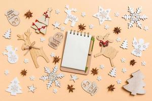 Festive decorations and toys on orange background. Top view of notebook. Merry Christmas concept photo