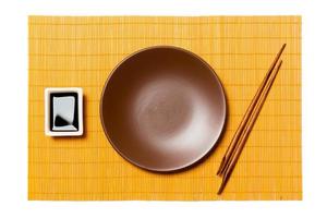 Empty round brown plate with chopsticks for sushi and soy sauce on yellow bamboo mat background. Top view with copy space for you design photo