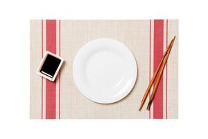 Empty round white plate with chopsticks for sushi and soy sauce on sushi mat background. Top view with copy space for you design photo