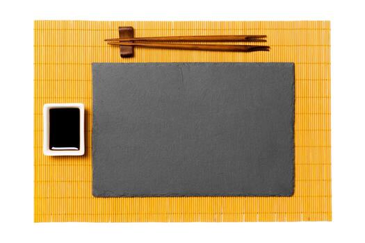 Empty rectangular black slate plate with chopsticks for sushi and soy sauce on yellow bamboo mat background. Top view with copy space for you design photo