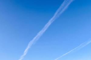 Aircraft condensation contrails in the blue sky inbetween some clouds photo