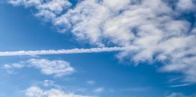 Aircraft condensation contrails in the blue sky inbetween some clouds photo