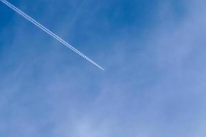 Aircraft condensation contrails in the blue sky inbetween some clouds photo