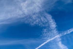 Aircraft condensation contrails in the blue sky inbetween some clouds photo