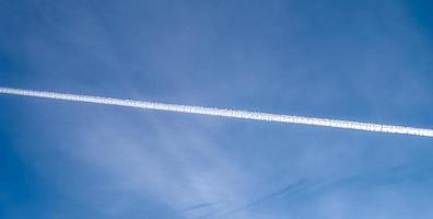 Aircraft condensation contrails in the blue sky inbetween some clouds photo