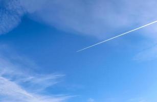 Aircraft condensation contrails in the blue sky inbetween some clouds photo