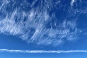 Aircraft condensation contrails in the blue sky inbetween some clouds photo