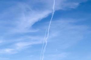 Aircraft condensation contrails in the blue sky inbetween some clouds photo